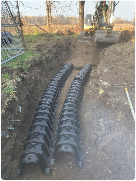 Installation and excavation of a septic system with 2 medium sized pipes underground near a field.